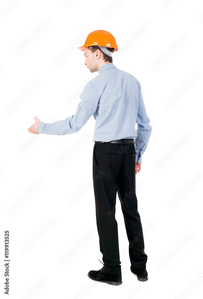 Backview of an engineer in construction helmet stands. Curly businessman in a light jacket and a helmet holds out his hand to the side for a handshake. Backview of an engineer in construction helmet stands. Curly businessman in a light jacket and a helmet holds out his hand to the side for a handshake.