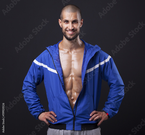 Smiling athletic man showing six pack abs on black background