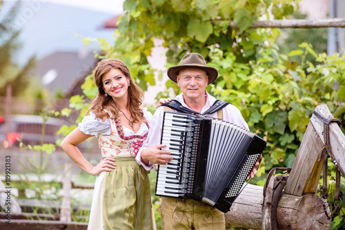 Fototapet Couple in traditional bavarian clothes with accordion, green gar