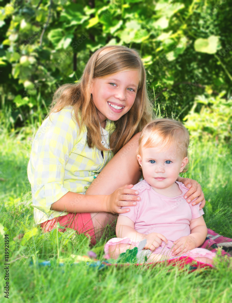 Two adorable sisters outdoors. Smiling girls sitting on the grass Two adorable sisters outdoors. Smiling girls sitting on the grass