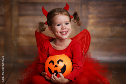 funny child girl in devil halloween costume on dark wooden back