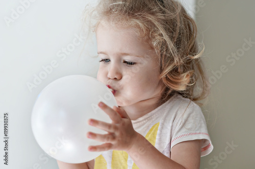 Adorable child girl is inflating a white balloon close-up