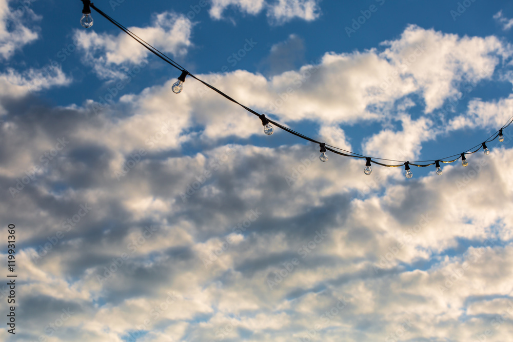 Lamp string hanging outside against a cloudy blue sky background