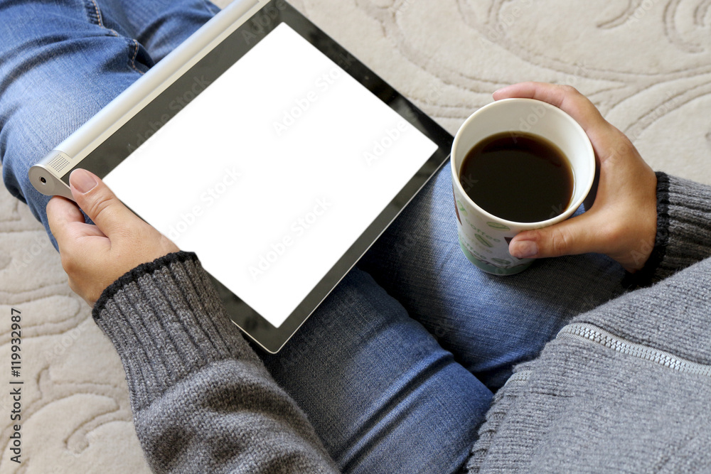 Obraz premium Young woman sitting and holding a tablet and a Cup of coffee . The concept of the online store. Shopping. Business of the house.Training.