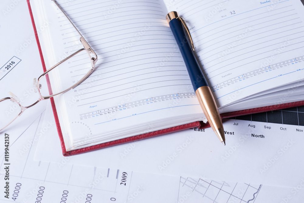 The business concept. Notebook, pen and glasses on top of financial charts The business concept. Notebook, pen and glasses on top of financial charts