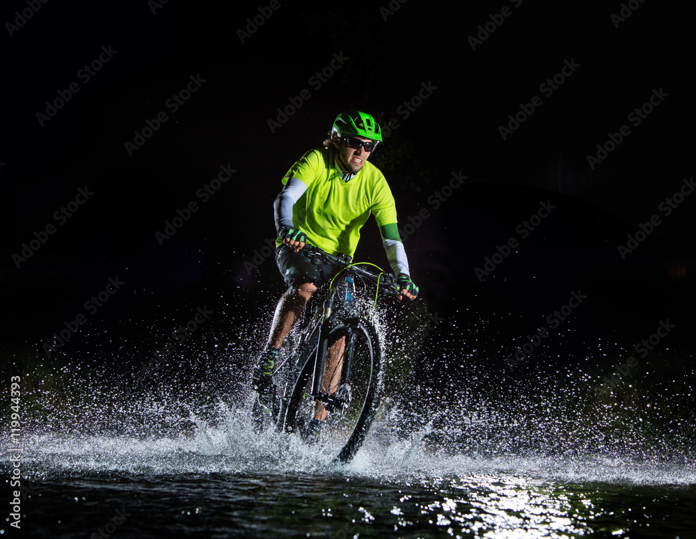 Mountain biker splashing in forest stream at night
