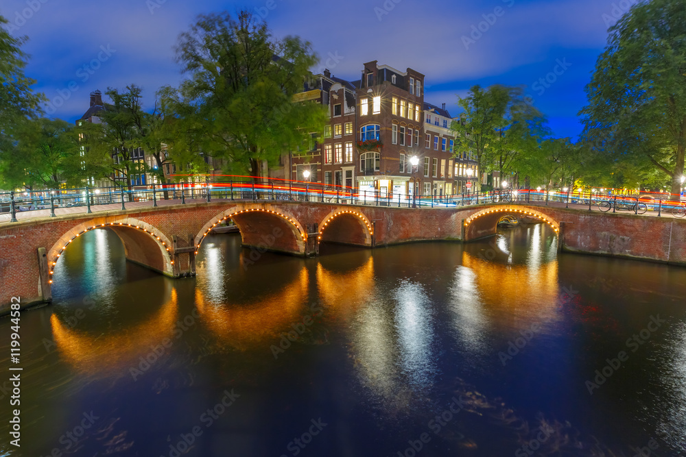 Amsterdam canal, bridge and typical houses, boats and bicycles during evening twilight blue hour, Holland, Netherlands.