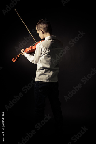 Rear view of boy with violin on black background