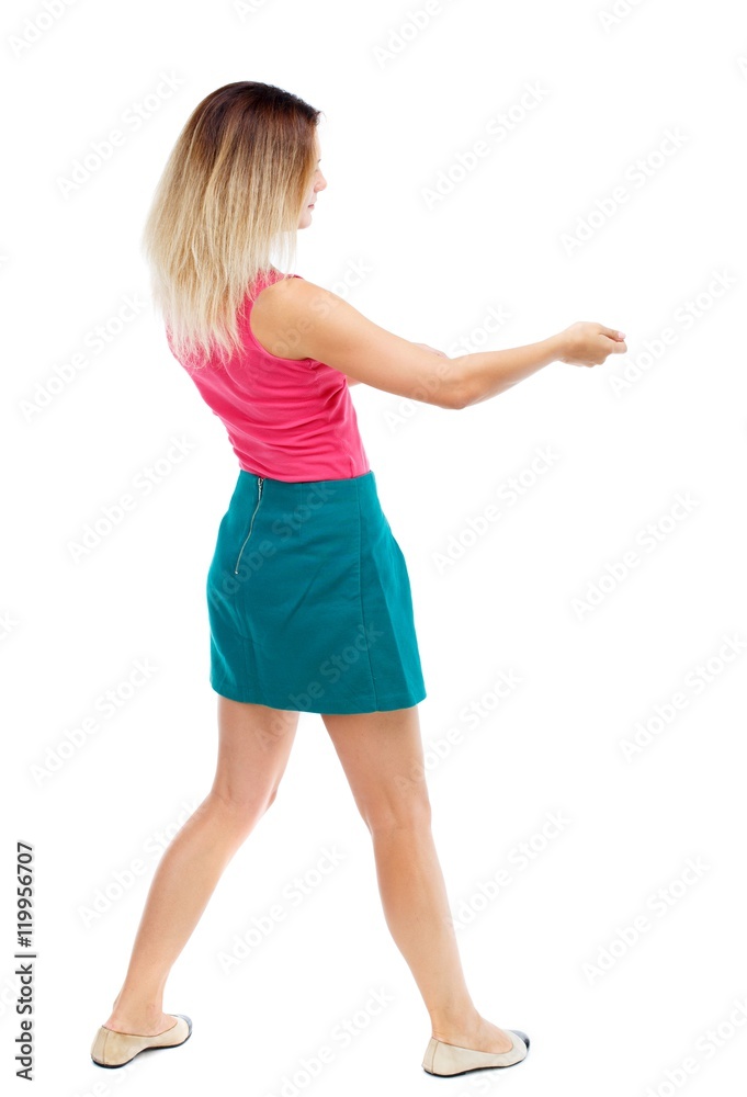 back view of standing girl pulling a rope from the top or cling to something. girl watching. Blonde in a red sweater and green skirt pulls the load on the rope. back view of standing girl pulling a rope from the top or cling to something. girl watching. Blonde in a red sweater and green skirt pulls the load on the rope.