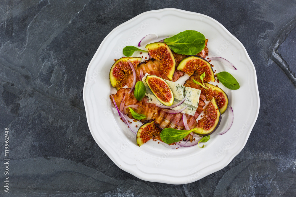 Figs and gorgonzola and fried bacon with small lettuce leaves served on a white plate.
Figs and gorgonzola and fried bacon with small lettuce leaves served on a white plate.