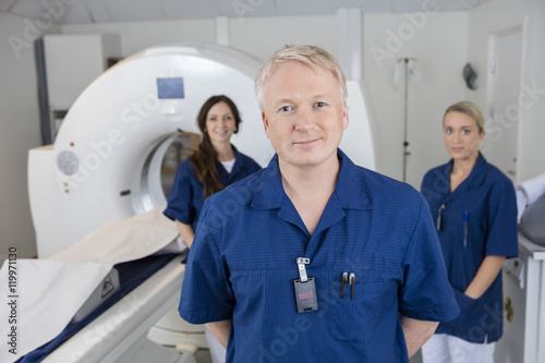 Confident Male Radiologist With Colleagues Standing By MRI Machi