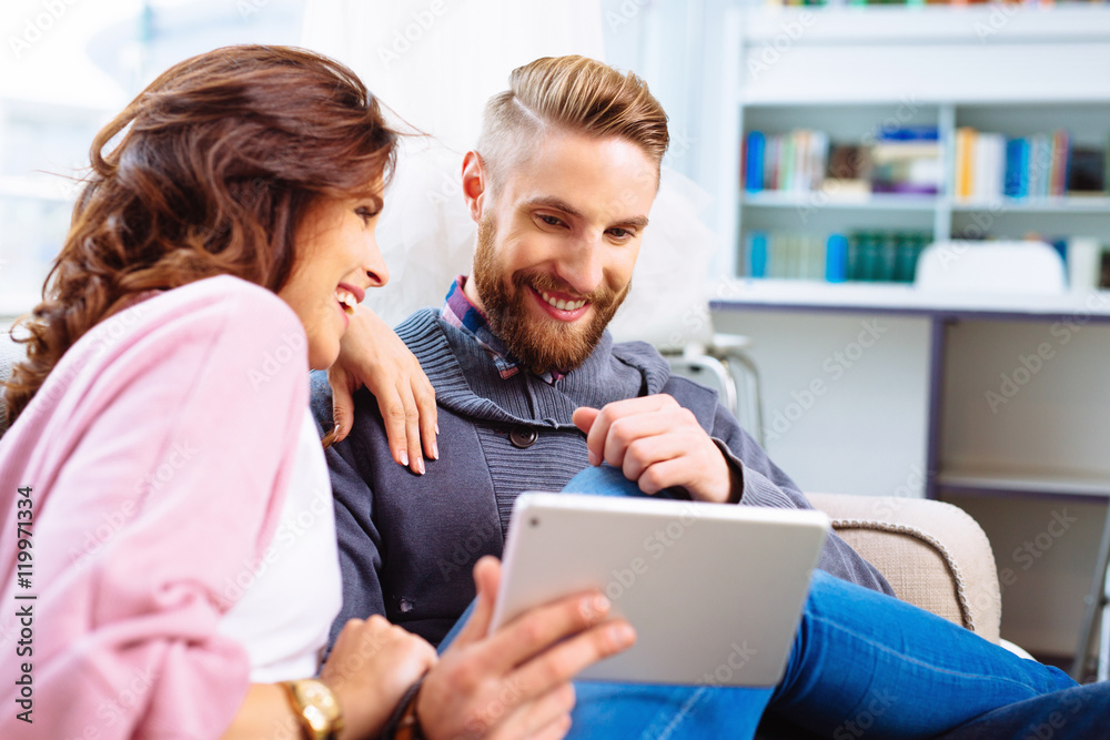 Happy couple browsing internet on digital tablet sitting togethe Happy couple browsing internet on digital tablet sitting togethe