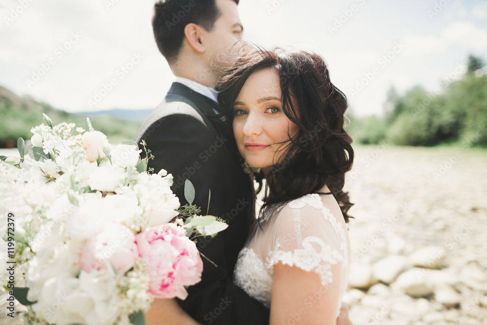 Close up portrait of couple against river and green trees. Beautiful young woman kissing handsome man outdoors Close up portrait of couple against river and green trees. Beautiful young woman kissing handsome man outdoors
