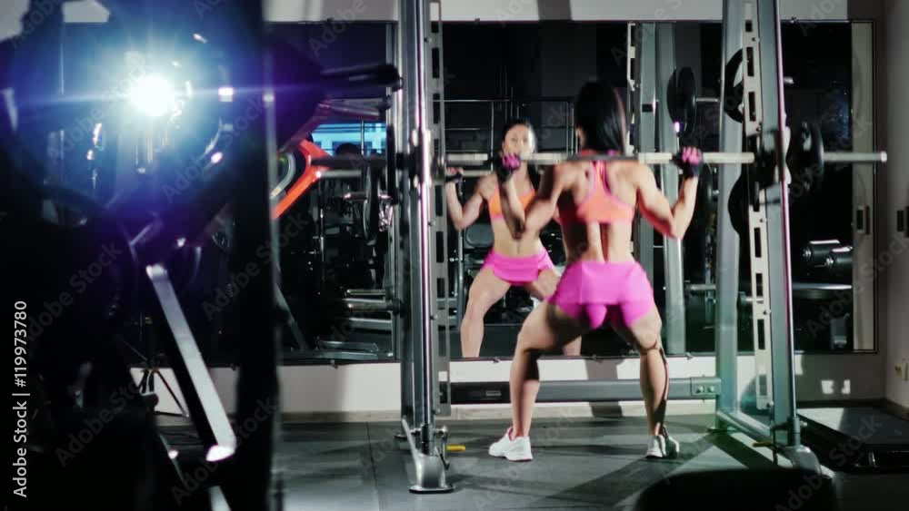 Athletic woman squats with a barbell. Motivation in sport. Back view Athletic woman squats with a barbell. Motivation in sport. Back view