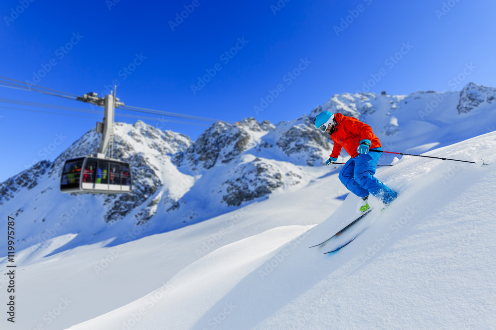 Skier skiing downhill in high mountains in fresh powder snow. Snow mountain range and cable railway in background. Mt Fort Peak Alps region Switzerland.