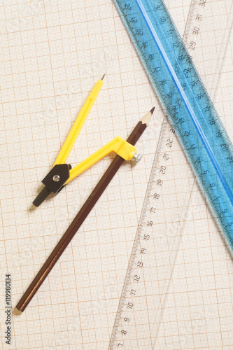 Yellow Drawing compass with black pensil and rulers on graph pa