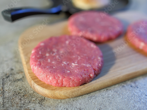 Crude cutlet of fresh meat, preparation for the burger on an old vintage wood board. Food and Cooking. Selective focus with shallow depth of field