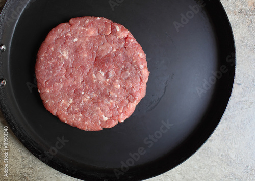Crude cutlet of fresh meat, preparation for the burger on an old vintage pan. Food and Cooking. Selective focus with shallow depth of field