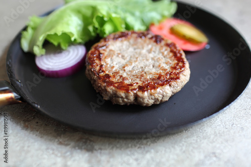 Vintage pan with fried juicy cutlet burger with slices of tomato and lettuce. Food and Cooking. Selective focus with shallow depth of field