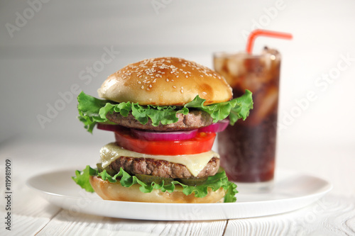 Big juicy traditional American burger with grilled meat and slices fresh vegetables closeup on a white plate on a wooden table. Food and beverages. Selective focus with shallow depth of field