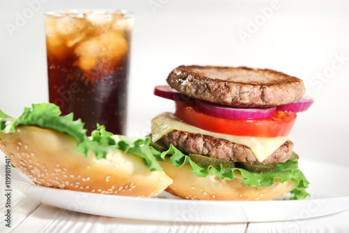 Big juicy traditional American burger with grilled meat and slices fresh vegetables closeup on a white plate on a wooden table. Food and beverages. Selective focus with shallow depth of field