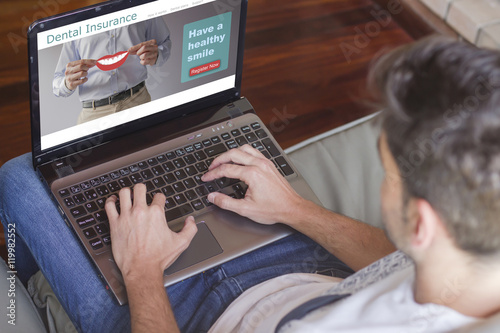 Close-up top view of young man at home typing the keyboard of a laptop with dental insurance plan on the screen.