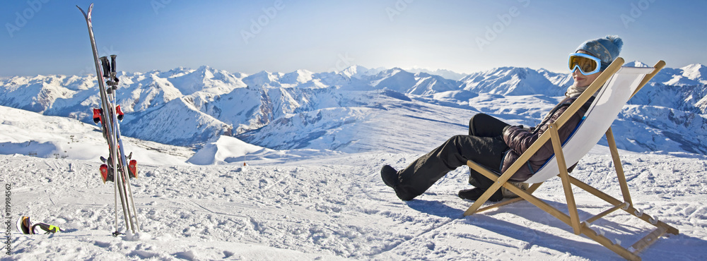 Panorama of a girl sunbathing in a deckchair near a snowy ski slope - obrazy, fototapety, plakaty 