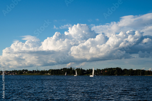 Widok na jezioro w po którym żeglują jachty. Na niebie widać rozbudowujące się chmury Cumulus.