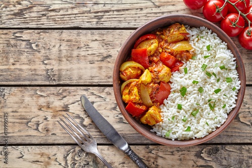 Chicken jalfrezi traditional homemade Indian spicy curry chilli meat with basmati rice and vegetables healthy dietetic asian food in clay dish on vintage table background.