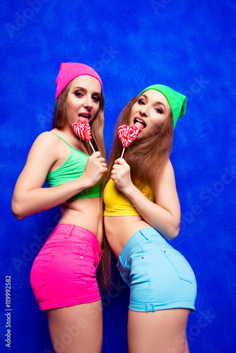 Two sexy slim women in color hats licking lollipops