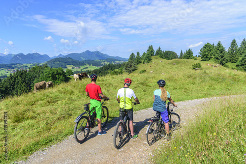 drei Radfahrer mit E-Bikes genießen die Aussicht im Allgäu