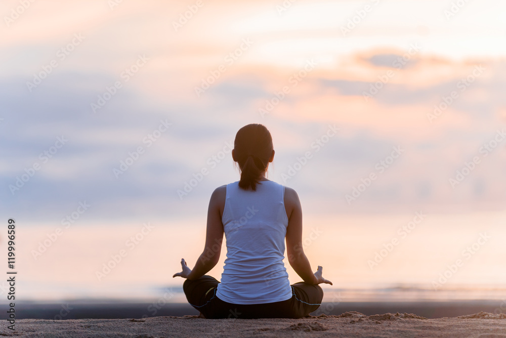 Young woman practicing yoga on the beach at sunset.