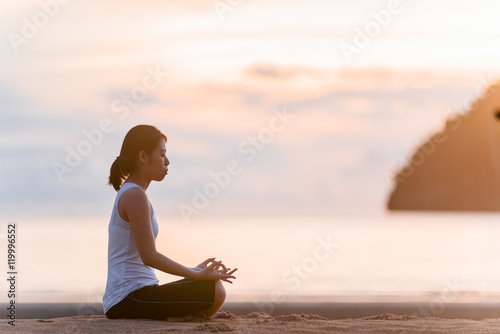 Young woman practicing yoga on the beach at sunrise.