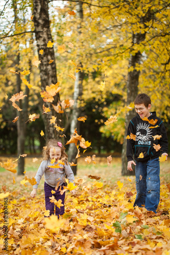 Brother and sister throwing leaves in autumn park © Olga Gorchichko