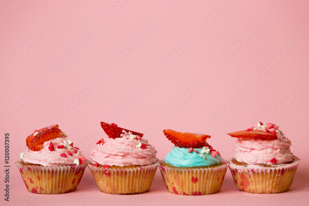 Pink and blue cupcakes with sprinkles and strawberries on pink b Pink and blue cupcakes with sprinkles and strawberries on pink b