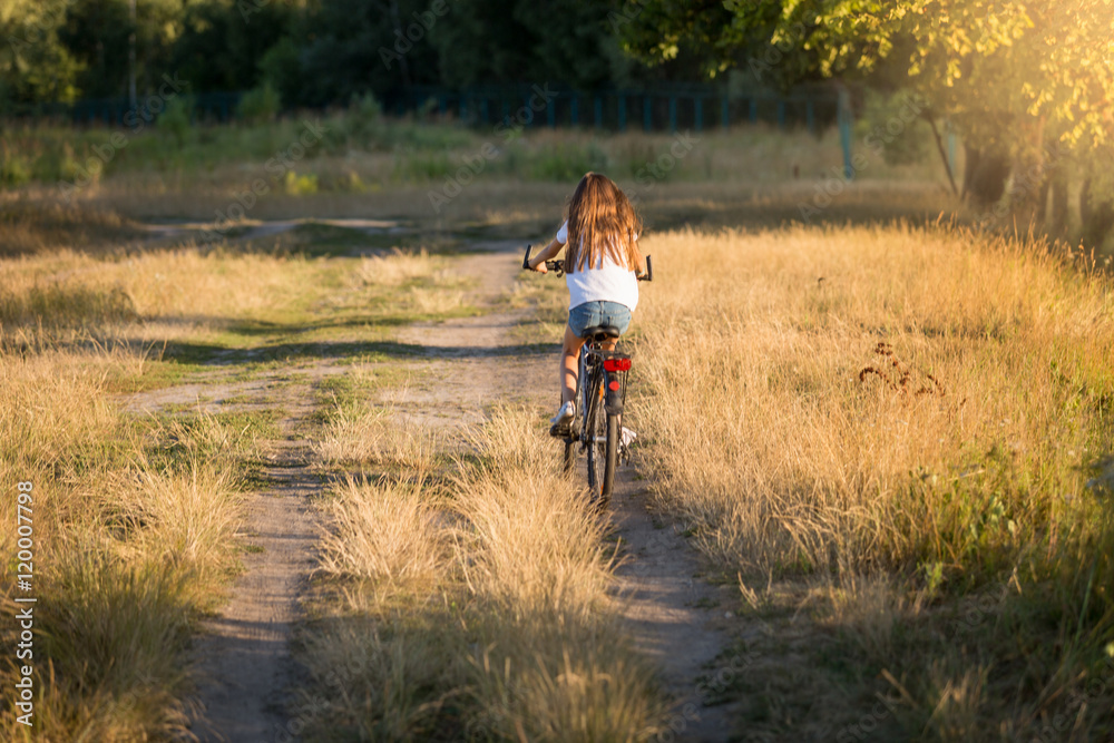 Obraz premium Woman riding bicycle on dirt road at meadow