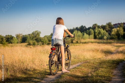 Fototapeta Naklejka Na Ścianę i Meble -  Girl in shorts and t-shirt cycling in meadow at sunset
