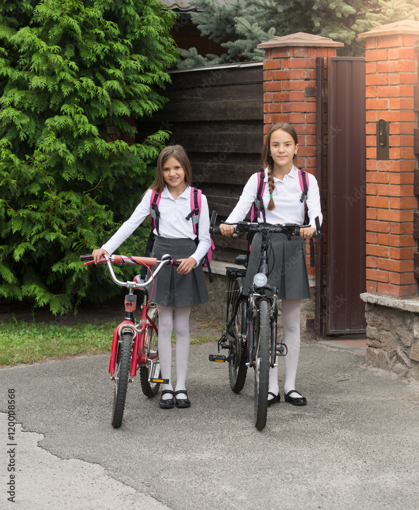 Obraz premium Smiling girls in school uniform with bicycles in front of house