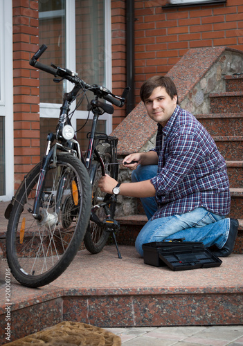 Man repairing bicycle on porch of his house