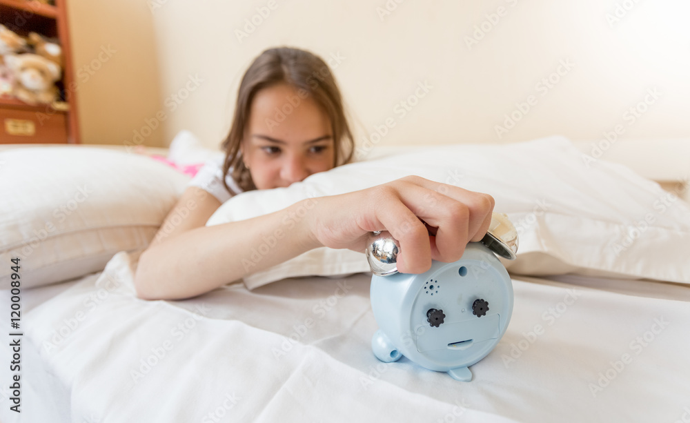 Closeup of annoyed girl reaching for alarm clock Closeup of annoyed girl reaching for alarm clock
