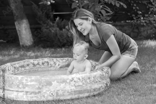 Black and white image of mother splashing with her baby boy at s