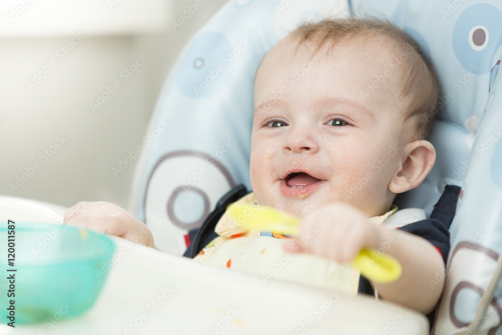 Cheerful smiling baby boy playing with spoon in highchair Cheerful smiling baby boy playing with spoon in highchair