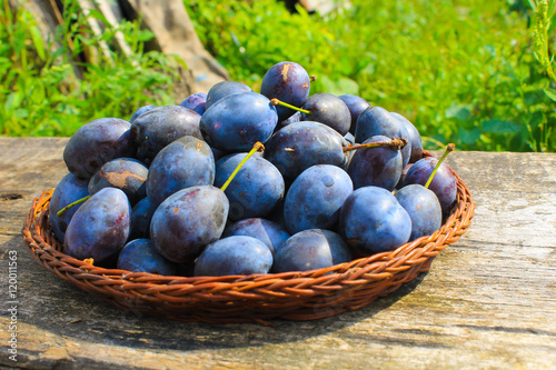 Fresh plums in rustic bowl on old wooden background