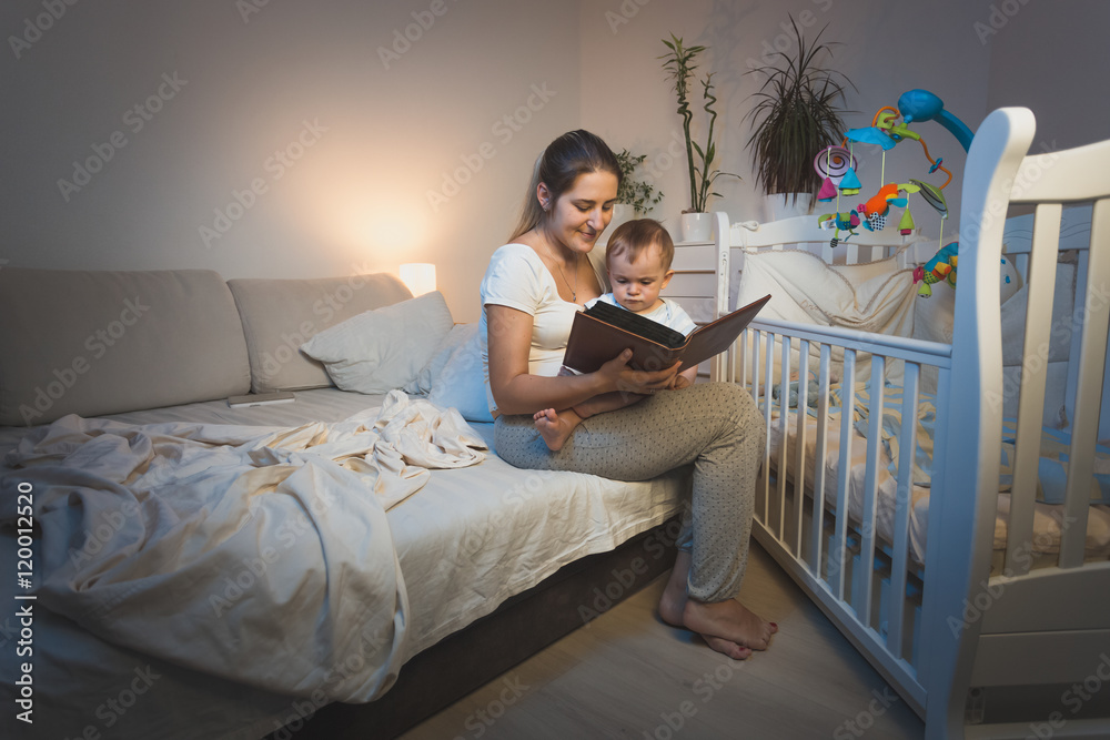 Φωτογραφία Portrait of mother holding baby boy on knees and reading him a b