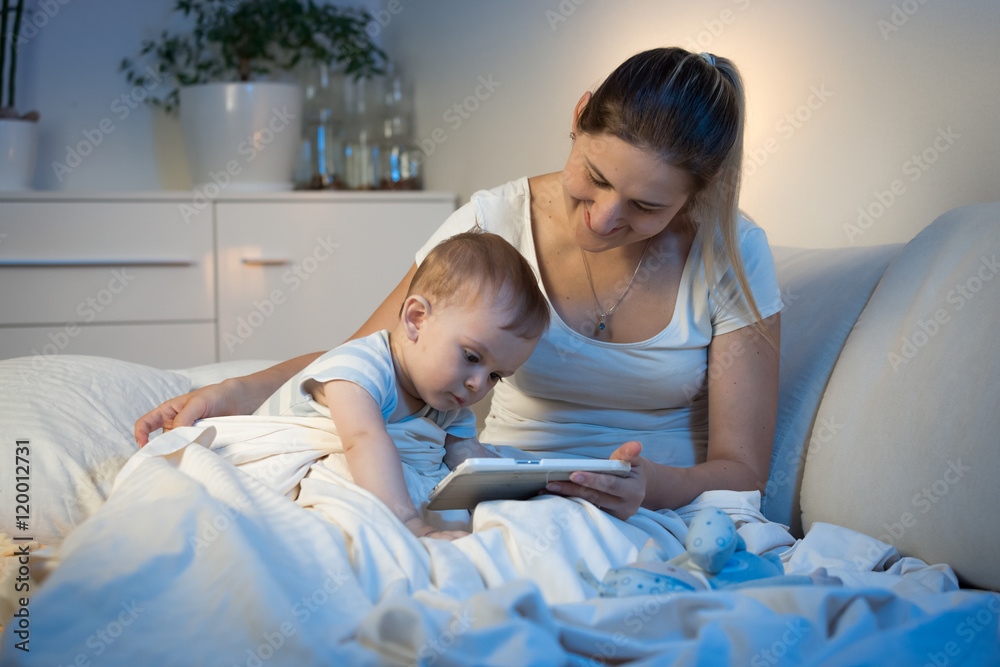 Baby boy sitting on bed with mother and using digital tablet at Baby boy sitting on bed with mother and using digital tablet at