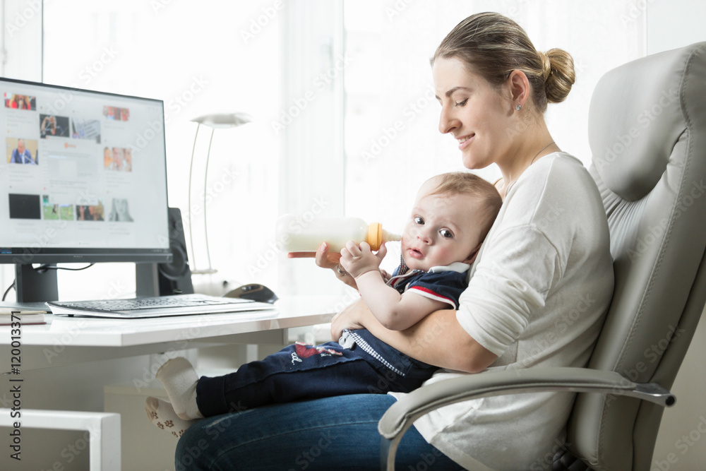 Beautiful woman feeding her baby from bottle while working at of Beautiful woman feeding her baby from bottle while working at of