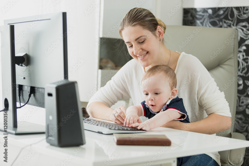 Beautiful smiling woman working on computer with her baby son Beautiful smiling woman working on computer with her baby son