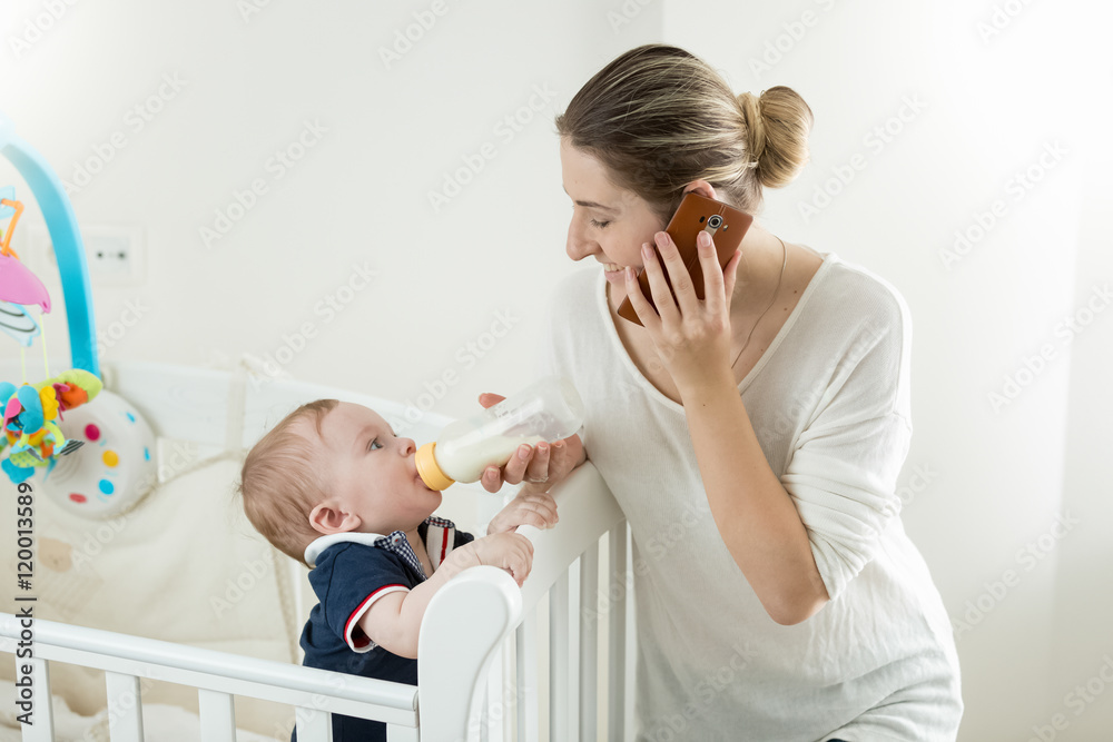 Φωτογραφία Portrait of mother talking by phone and feeding her baby from bo