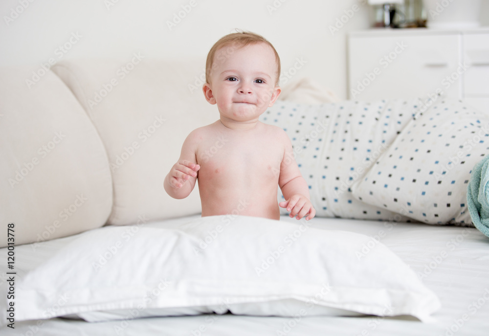 Naked baby boy sitting on bed at bedroom