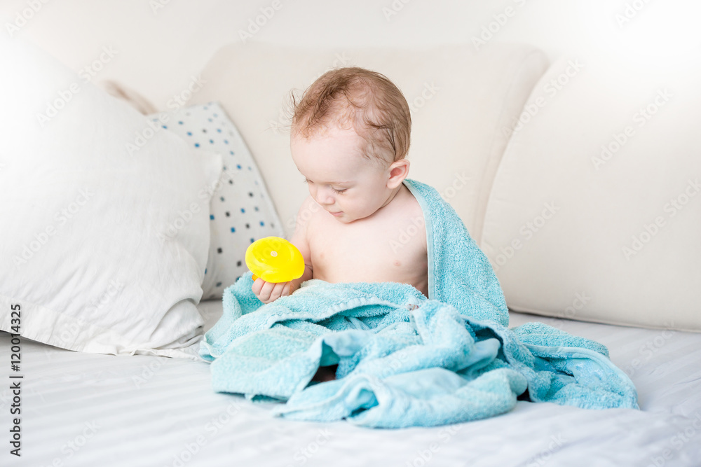 Foto Baby boy covered in blue towel playing with yellow rubber duck o